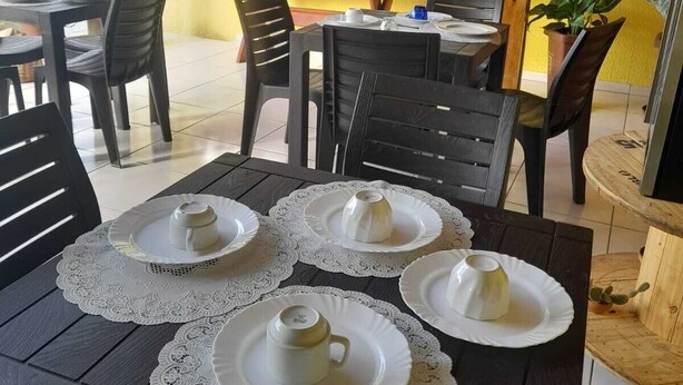 An outdoor dining area with tables set for four, chairs, and a yellow wall with a lattice design. - Pousada Terrissol (São Gonçalo do Amarante)
