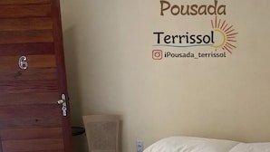 A hotel room with a bed, white towels, a wooden door, and a wall with the hotel's logo and Instagram handle. - Pousada Terrissol (São Gonçalo do Amarante)