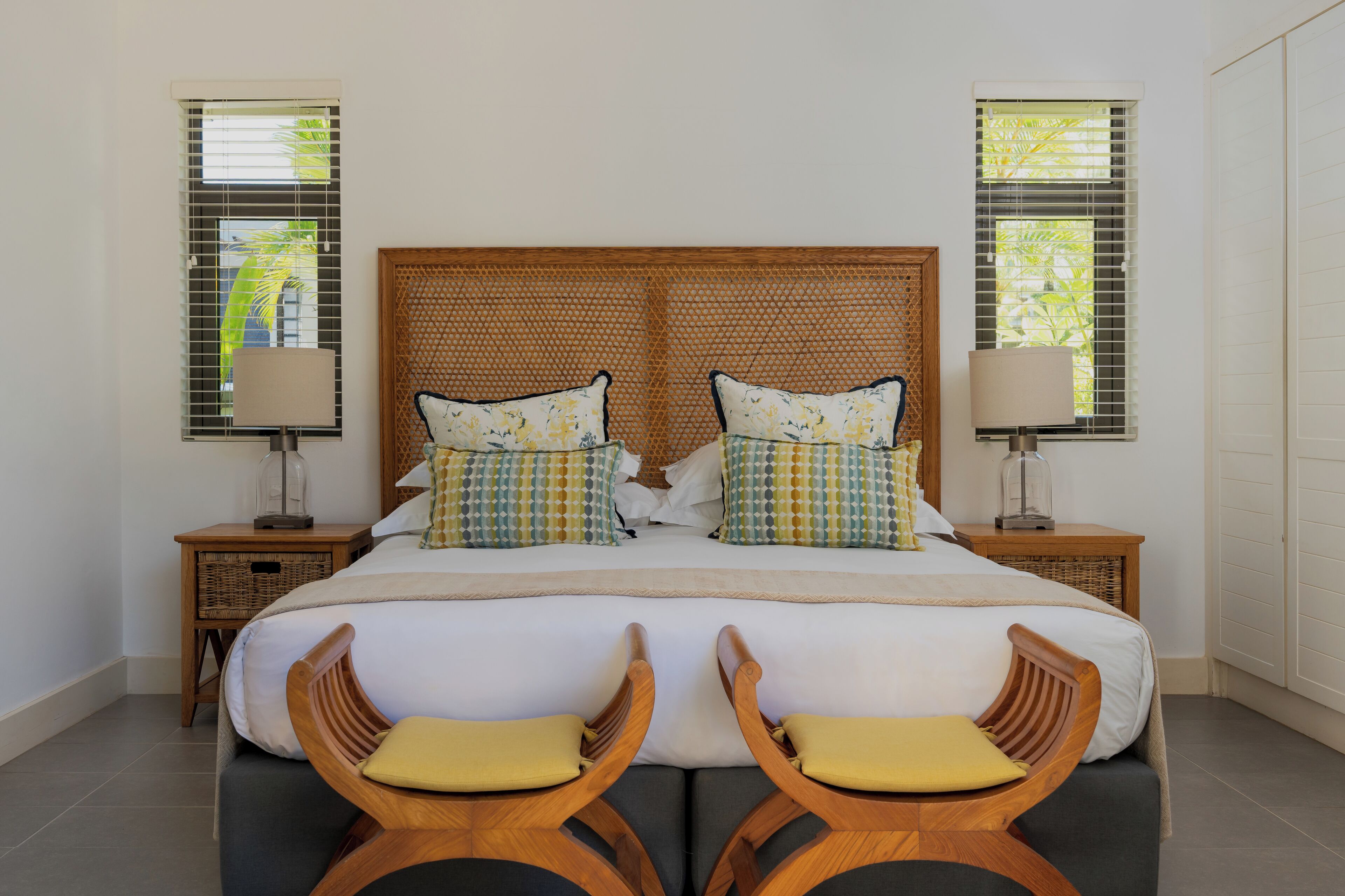 A double bed with a woven headboard, two nightstands with lamps, and two wooden chairs with cushions.