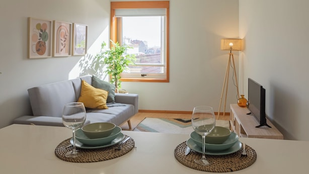 A modern living room with a sofa, a dining table set with plates and glasses, a floor lamp, and a TV. - Edifício Vencedor (Matosinhos)