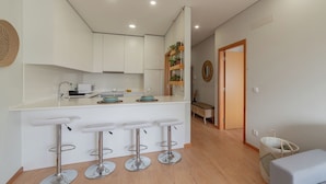 A modern kitchen with white cabinets, a central island with bar stools, and a hanging plant shelf. - Edifício Vencedor (Matosinhos)