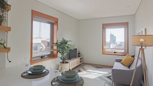 A modern living room with a sofa, TV, and dining area with plates and glasses. - Edifício Vencedor (Matosinhos)
