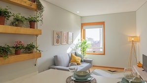 A living room with a sofa, a dining table with plates and glasses, a lamp, and potted plants on shelves. - Edifício Vencedor (Matosinhos)