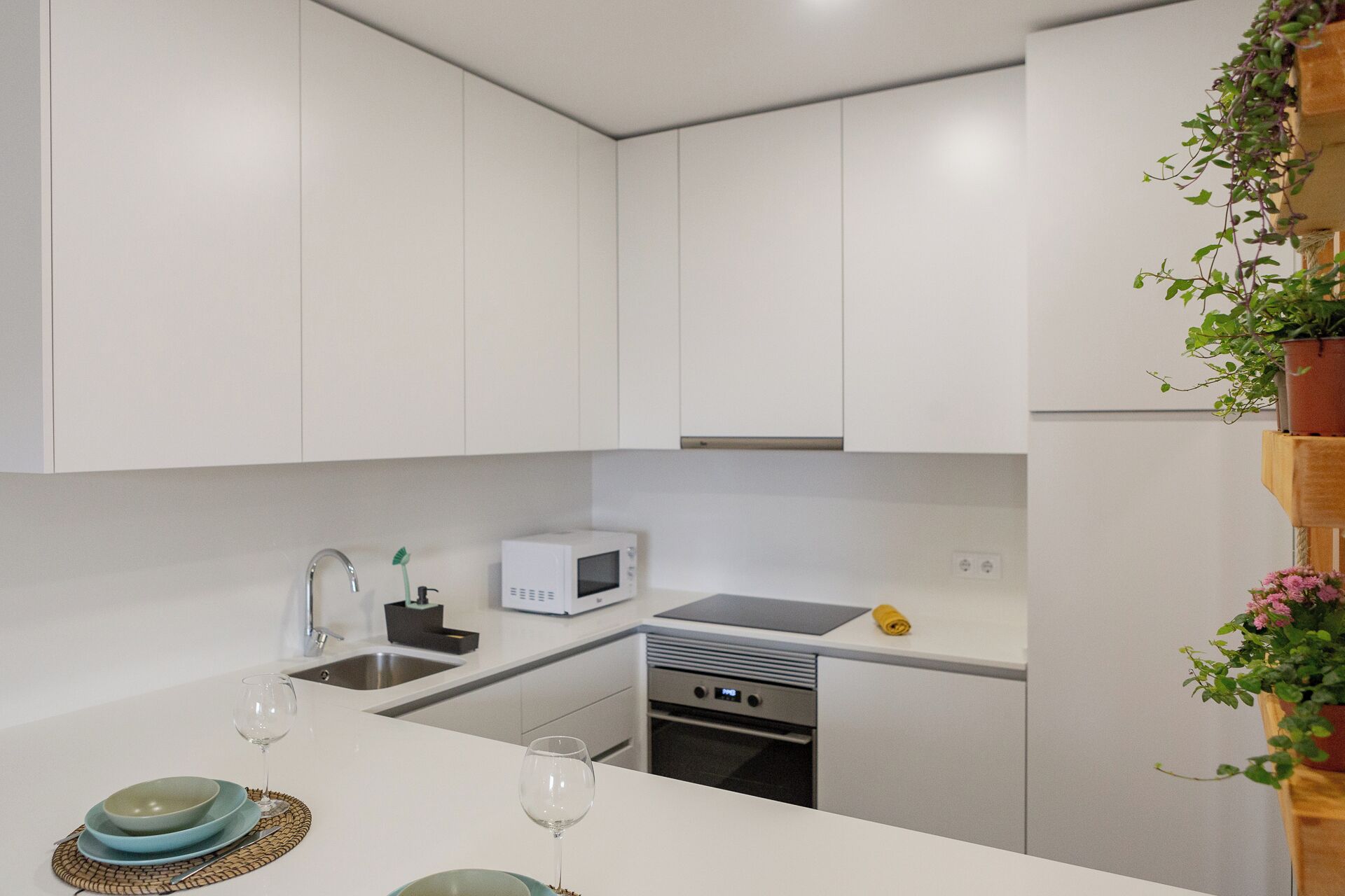 Una cocina moderna con armarios blancos, microondas, un lavamanos y un horno pequeño.