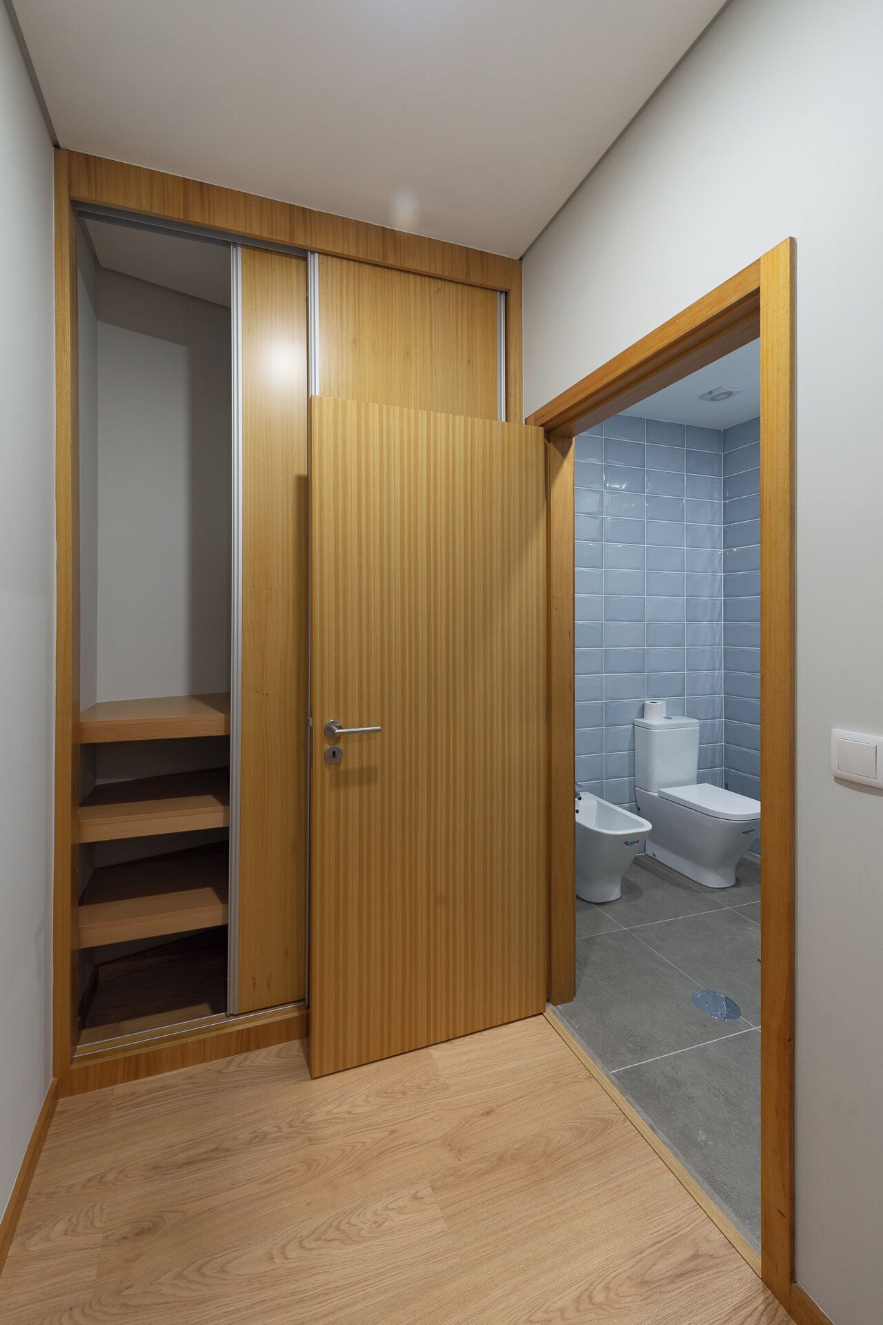 A room with a wooden wardrobe, a bathroom with a toilet and bidet, and a wooden floor.