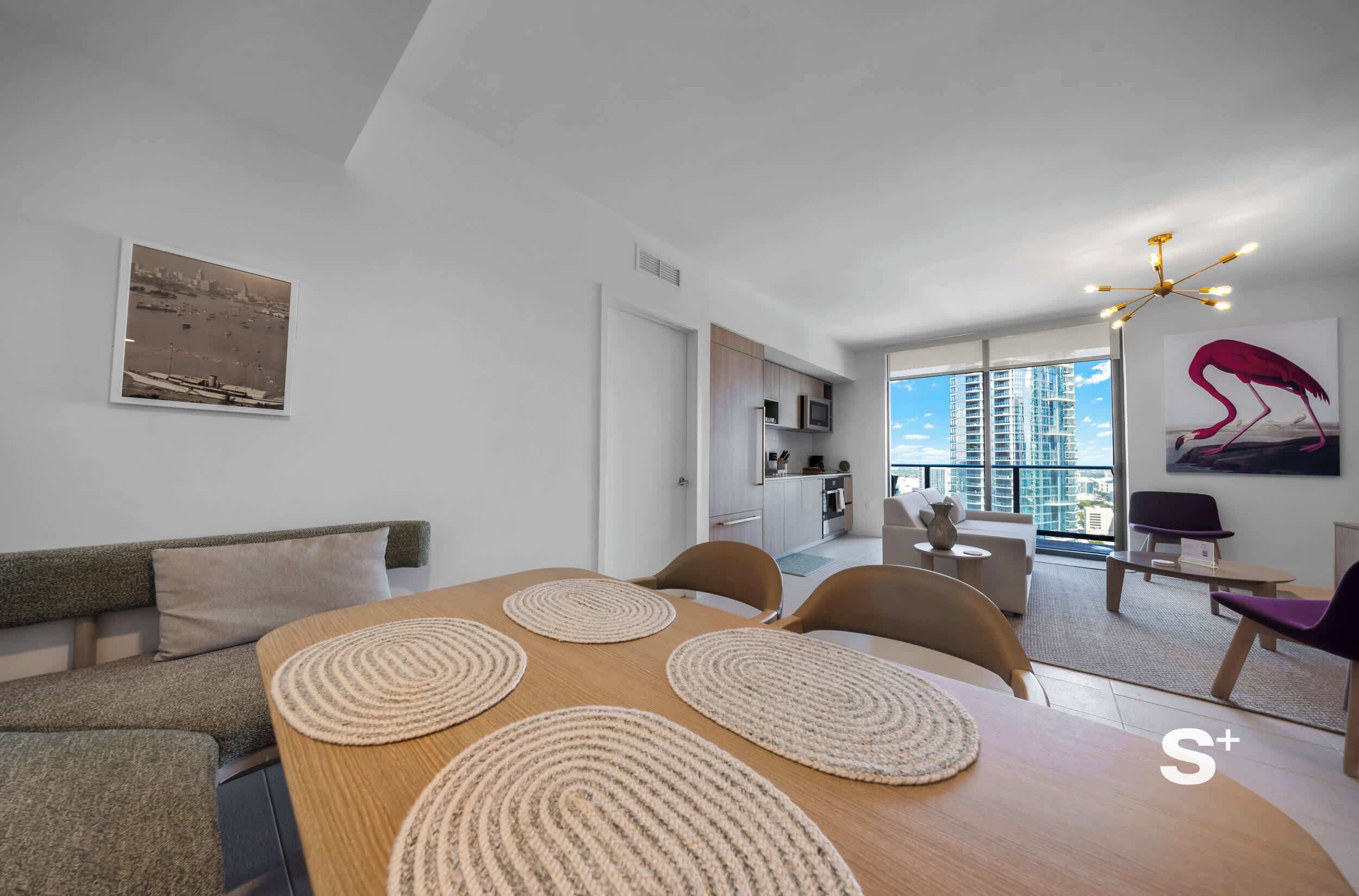 Una sala de estar moderna con una mesa de comedor, sofá y vistas a un paisaje urbano a través de grandes ventanales.