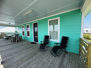 A covered outdoor deck with wooden benches and chairs, a table, and a door.