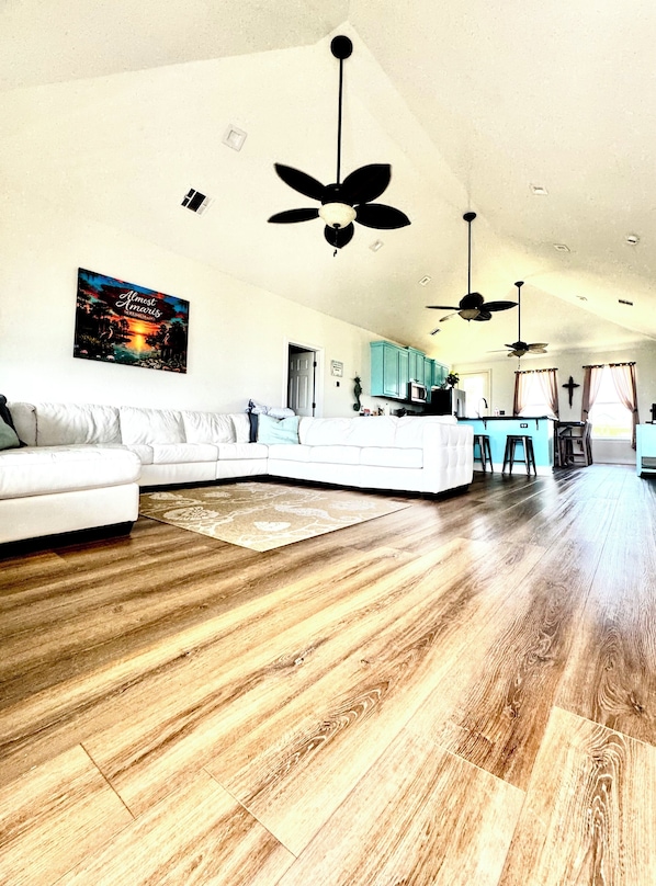 A spacious living area with a white sofa, wooden flooring, and ceiling fans.