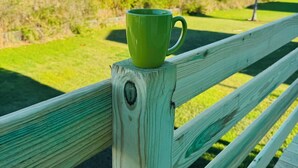 Eine grüne Tasse auf einer Holzbank, im Hintergrund Häuser und Palmen bei freier Sicht.