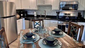 Una cocina moderna con gabinetes blancos, electrodomésticos de acero inoxidable y una mesa de comedor de madera para cuatro personas.