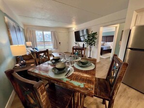 A dining area with a wooden table set for two, a television mounted on the wall, and a kitchen area visible in the background. - Couple’s Getaway-Pools/Gym/Branson Landing (Branson)