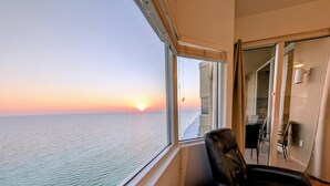 A balcony with a view of the sea at sunset, a chair, and a small table with starfish and a turtle decoration. - Luxe Tidewater Penthouse sleeps 10 (Panama City Beach)