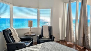 A room with a bed, two chairs, a lamp, and large windows with a view of the sea. - Luxe Tidewater Penthouse sleeps 10 (Panama City Beach)
