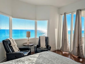 A room with a bed, two chairs, a lamp, and large windows with a view of the sea. - Luxe Tidewater Penthouse sleeps 10 (Panama City Beach)
