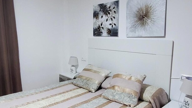Ein Hotelzimmer mit Bett, Nachttisch, Lampe, Klimaanlage und zwei Wandbildern.