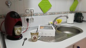 Eine Küche mit Kaffeemaschine, Wasserkocher, Tasse, einer mit 'TEE' beschrifteten Schachtel und einem Spülbecken.