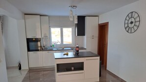 A modern kitchen with white cabinets, a black countertop, a built-in oven, and a window. - Apartment Freya (Karlovac)