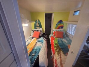 Une chambre avec deux lits, chacun doté d’une tête de lit au design unique, une porte donnant sur une autre pièce et une petite fenêtre.
