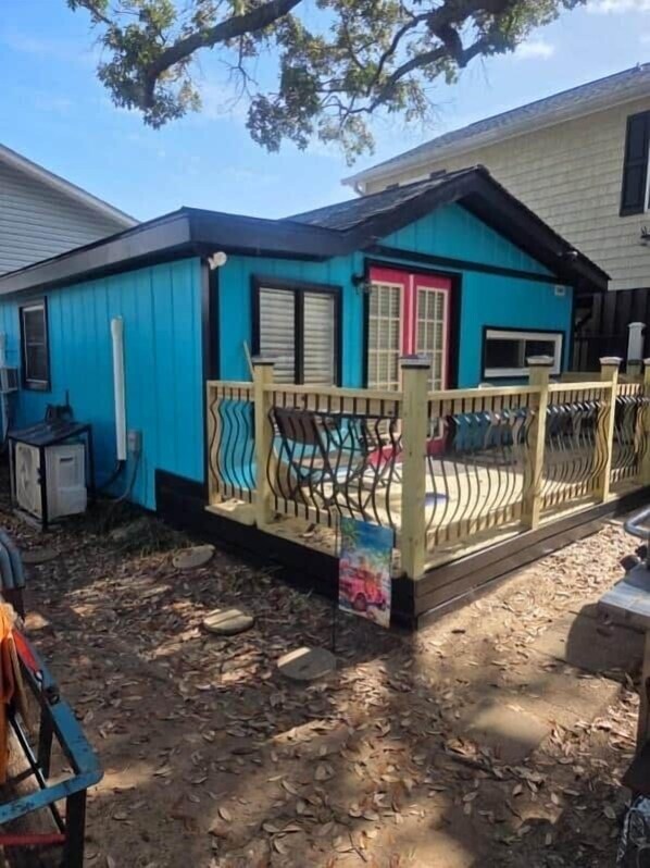 Une maison bleue avec une véranda entourée d’une clôture, une porte rose et une petite table.