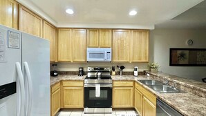 Una cocina con armarios de madera, microondas, estufa, refrigerador y un lavamanos.