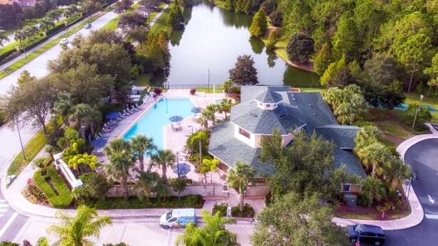 Vista aérea de una zona residencial con piscina, una casa de diseño arquitectónico singular y un lago rodeado de árboles.