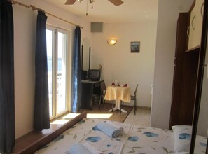 Une chambre à coucher comprenant un lit, un bureau, une chaise, un téléviseur et une petite table recouverte d’une nappe.