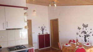 A kitchen with a stove, cabinets, and a dining area with a table set for two. - Azure Hvar Residence (Hvar)