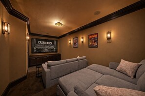 A home theater room with a large flat-screen TV, two couches, and wall-mounted speakers. - Heights Retreat | Heated Pool/Spa | Elevator (Houston)