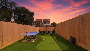 Een achtertuin met kunstgras, een tafeltennistafel en een pooltafel.