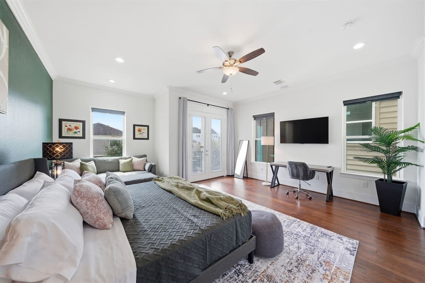 A modern bedroom with a bed, a desk, a chair, a TV, and a large window.