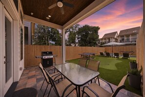 Una terrazza esterna con tavolo e sedie, un barbecue e vista su una zona residenziale al tramonto.