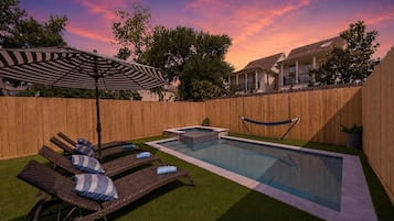Un patio trasero con piscina, sillas de descanso y un cerco de madera.