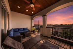 A balcony with a sofa, wicker furniture, and a view of the cityscape at sunset. - Heights Retreat | Heated Pool/Spa | Elevator (Houston)