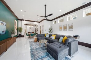 A spacious living area with a grey sectional sofa, a coffee table, and a dining area with a wooden table and chairs. - Heights Retreat | Heated Pool/Spa | Elevator (Houston)