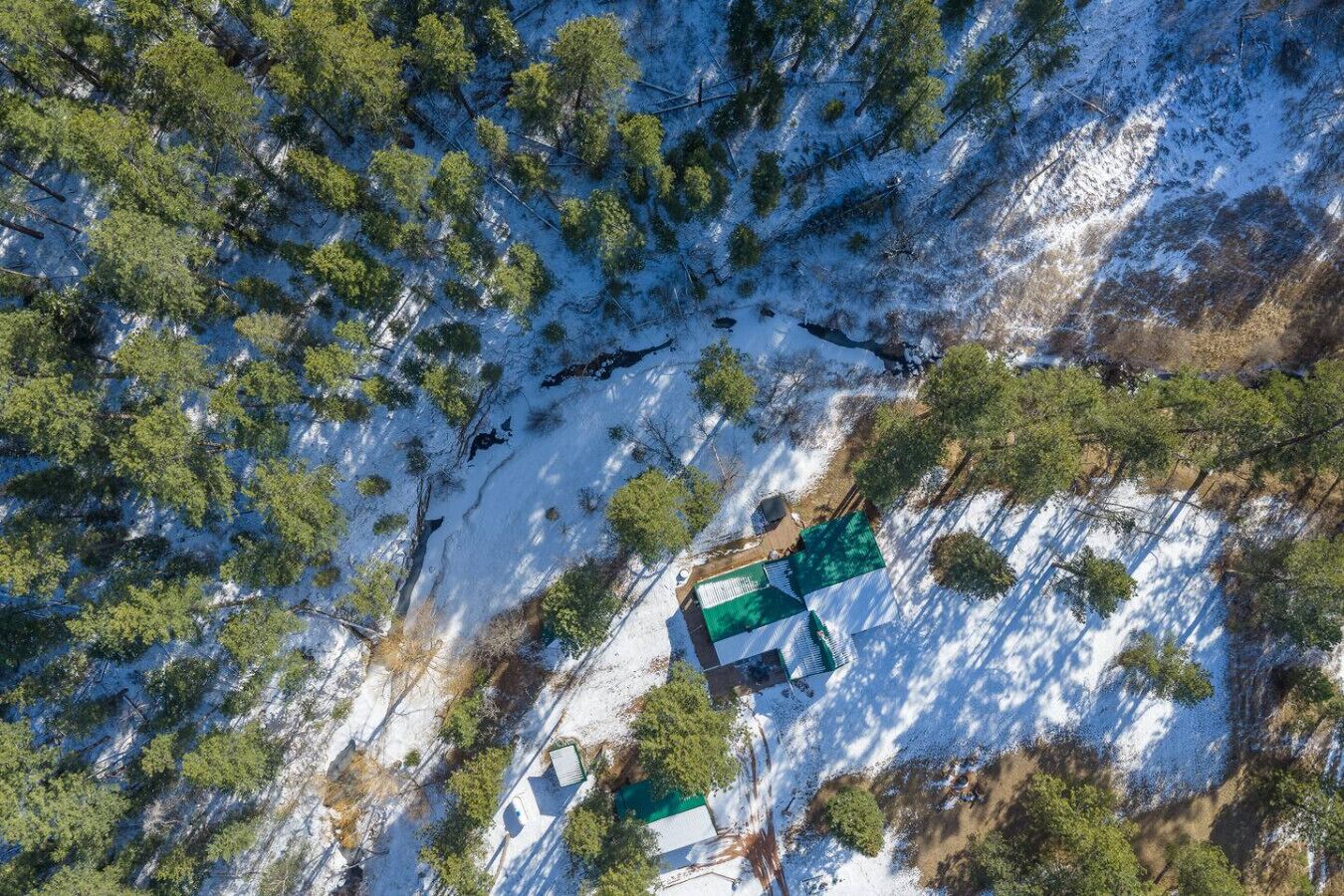 Vista aérea de una cabaña rodeada de árboles y con el suelo cubierto de nieve.