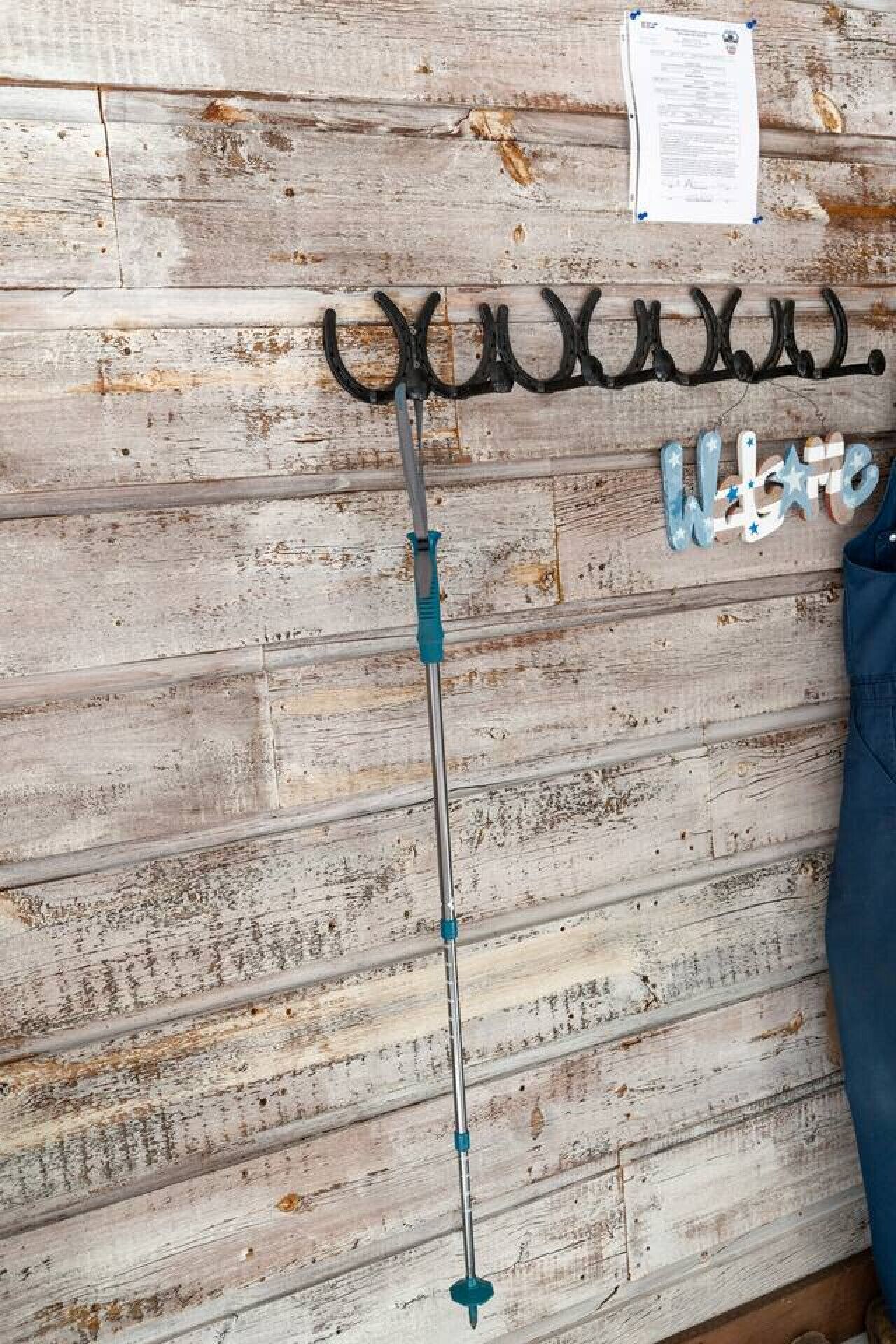 Un porte-manteau en métal sur lequel est accroché un manteau, un mur en bois à la texture patinée et une feuille de papier fixée au mur.