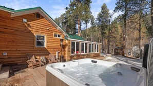 Eine Holzhütte mit Whirlpool, einer Holzterrasse und Blick auf einen Wald.
