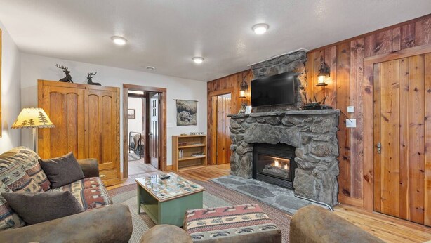 Ein gemütliches Wohnzimmer mit Kamin aus Stein, Holzwänden, einem Fernseher und einer Couch mit gemusterten Kissen.