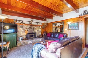 Een gezellige woonkamer met een stenen openhaard, leren bank, houten balken en een opgeplakt hertengestalte.