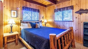 Una habitación de cabaña de madera con una cama, dos lámparas, una chimenea y una ventana con vistas.