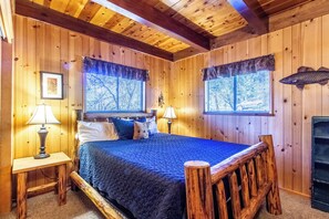 Ein Zimmer in einer Holzhütte mit einem Bett, zwei Lampen, einem Kamin und einem Fenster mit Blick.