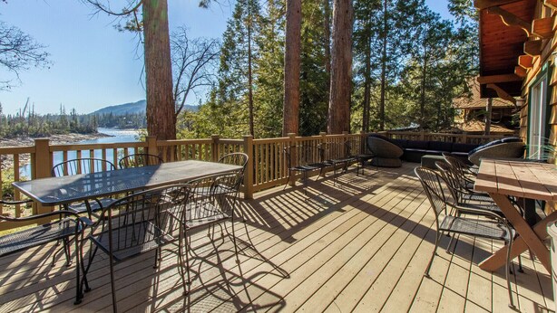 Terraza de madera con muebles de exterior, con vistas a un lago y un bosque.