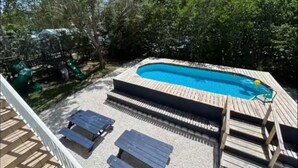 Patio trasero con piscina, terraza de madera y mobiliario exterior.
