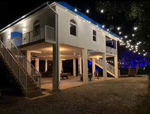 A two-story building with outdoor seating areas, a staircase, and string lights. - Casa en los Cayos de Florida. (Key Largo)