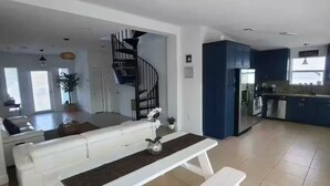 Un área de estar amplia con un banco blanco, una escalera y una zona de cocina.