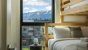 Ein Schlafzimmer mit einem Etagenbett, Blick auf Berge durch ein großes Fenster und einem kleinen Tisch mit einer Lampe.