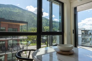 A room with a large window, a table with a bowl, and a chair. - Rest & Roam in Mackenzie Village (Revelstoke)