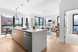 A modern kitchen with a central island, a dining area with a sofa and coffee table, and large windows offering views of the city. - Rest & Roam in Mackenzie Village (Revelstoke)