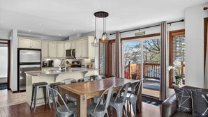 A modern kitchen with a central island, stainless steel appliances, and a dining area with a wooden table and gray chairs.