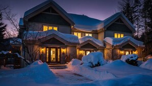 A two-story house with a snow-covered roof and driveway, surrounded by trees.